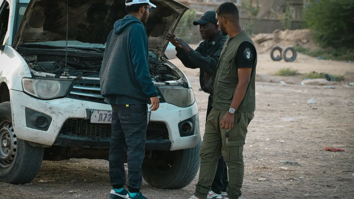 Trois hommes examinent une voiture, capot ouvert